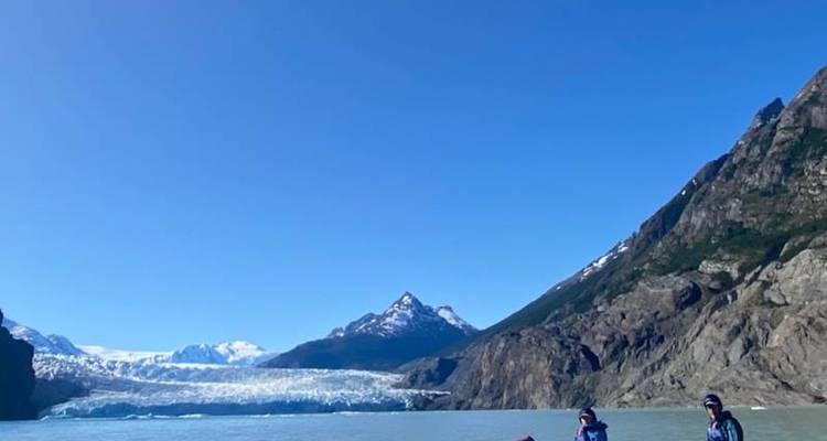 Los kayakistas remar en un lago glacial lechoso rodeado de empinadas montañas rocosas bajo un cielo azul.