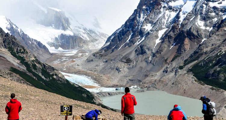 Los excursionistas hacen una pausa en un paso elevado con vistas a un valle glacial y un lago lechoso abajo.