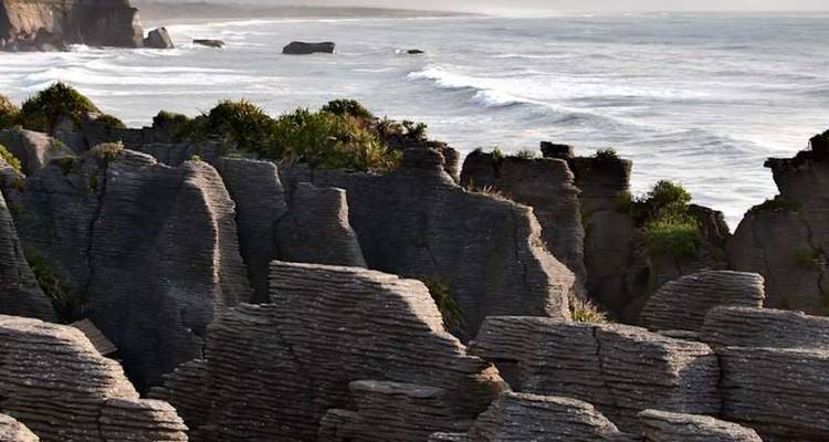 Formations calcaires érodées le long d'une côte accidentée avec des vagues s'écrasant à la lumière du soir.