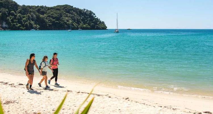 Trois randonneurs marchent le long d'une plage de sable blanc blanc à côté d'une mer turquoise par une journée ensoleillée.