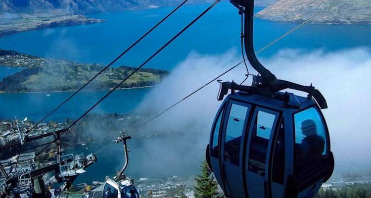 Le téléphérique monte au-dessus de Queenstown, révélant un panorama du lac et une vallée remplie de brouillard.