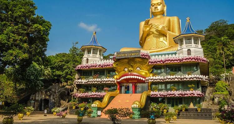 Massive goldene Buddha-Statue auf der farbenfrohen Fassade des Goldenen Tempels von Dambulla unter blauem Himmel.