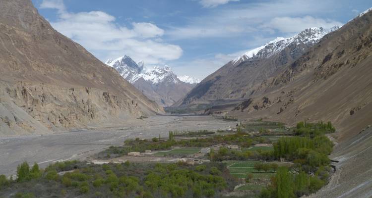 Green valley settlements sit between barren canyon walls with snow-clad giants in the distance.