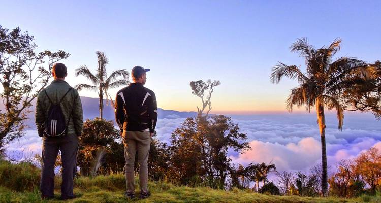 Deux randonneurs se tiennent sur une crête herbeuse surplombant une mer de nuages et des montagnes lointaines à l'aube.