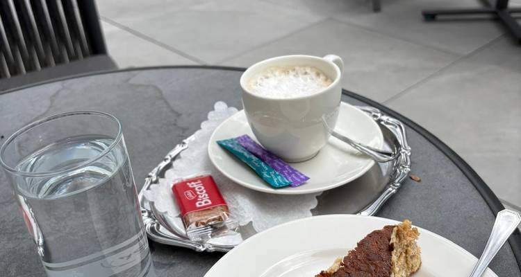 Gros plan d'un cappuccino, d'un biscuit et d'une part de gâteau sur une table de café en plein air.