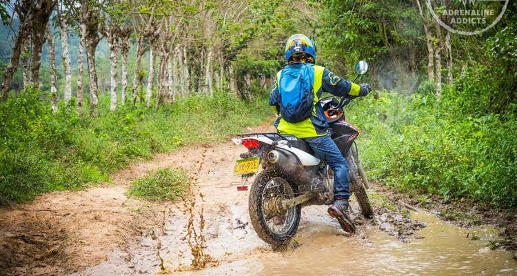 Fahrer, der einen schlammigen Waldweg durchfährt, während Wasser um das Motorrad spritzt.