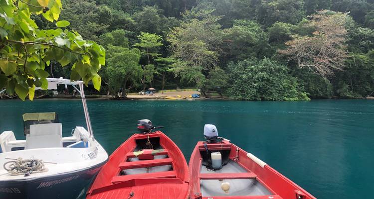 Des bateaux rouges et blancs amarrés sur une eau d'un bleu éclatant avec une forêt dense en arrière-plan