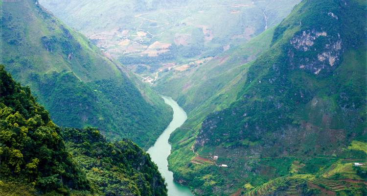 El río turquesa serpentea a través de un cañón verde y empinado con granjas en terrazas en las laderas de las montañas.