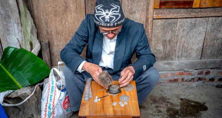 Anciano artesano con gorro de punto puliendo meticulosamente monedas en un pequeño banco de trabajo de madera.