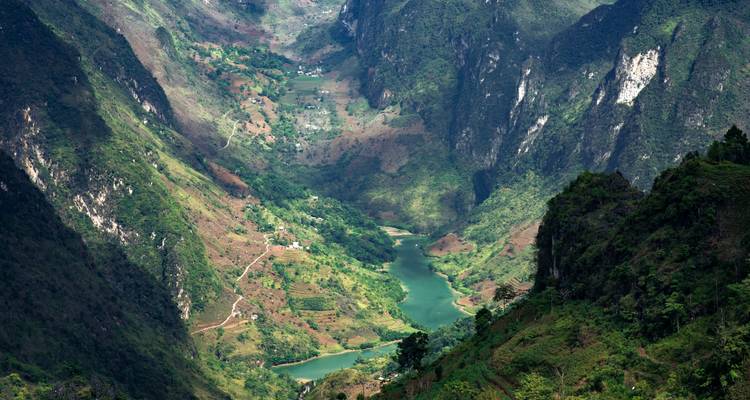 Punto de vista elevado sobre un cañón profundo con río esmeralda, acantilados escarpados y granjas dispersas.