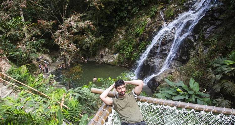 Un hombre se relaja en una plataforma de hamaca sobre una piscina de la selva con una cascada en el fondo.