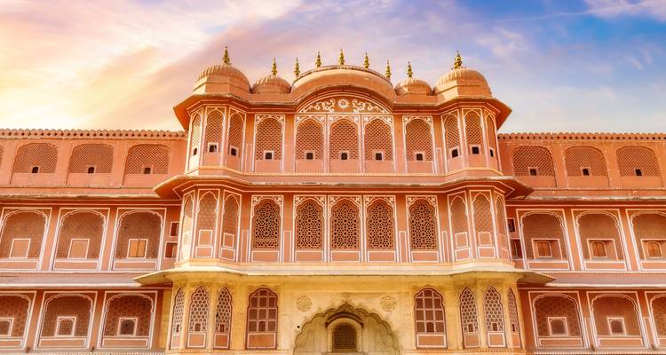 La fachada de piedra arenisca rosa simétrica del Palacio de la Ciudad de Jaipur brilla bajo un cielo cálido.