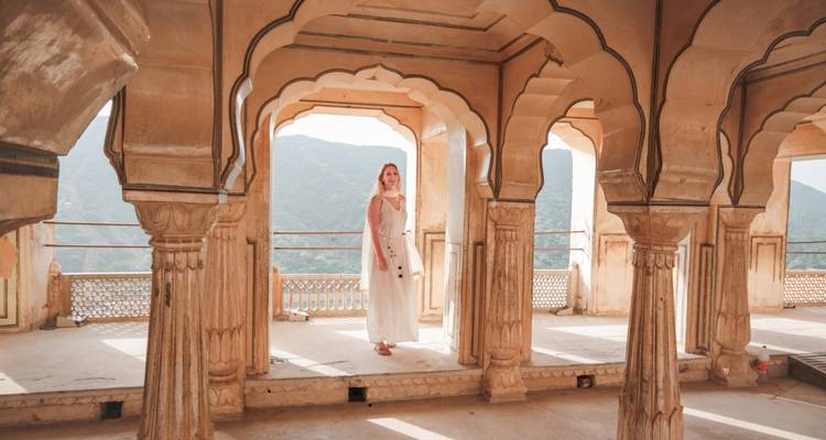 Una mujer con un vestido blanco se encuentra entre columnas de arenisca arqueadas mirando hacia colinas cubiertas de bosque.