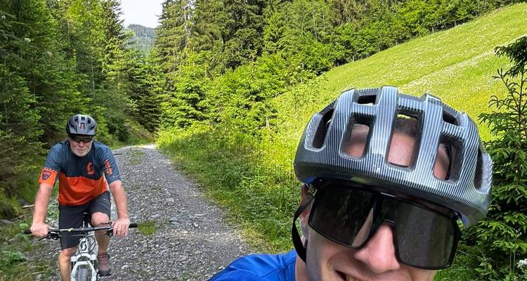 Photo style autoportrait de deux vélotouristes circulant sur un sentier forestier rocailleux dans une forêt alpine luxuriante