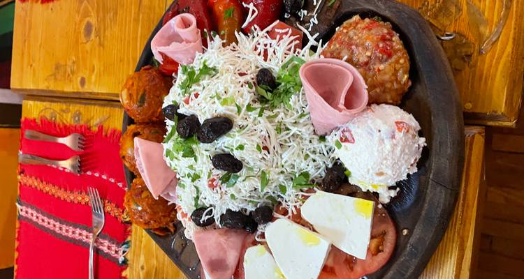 Een houten bord vol Bulgaarse salades, kazen, ham en groenten op een rustieke tafel.