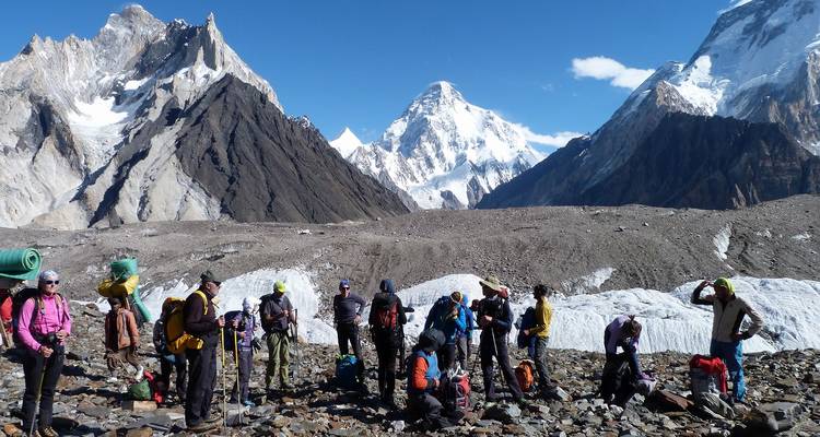 Groupe de randonneurs avec sacs à dos et bâtons se reposant sur la moraine rocheuse sous les pics enneigés imposants du Karakoram.
