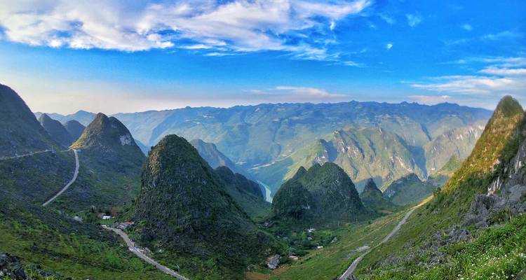 Una vista panorámica impresionante de montañas verdes escarpadas y carreteras sinuosas bajo un cielo azul brillante en el norte de Vietnam.