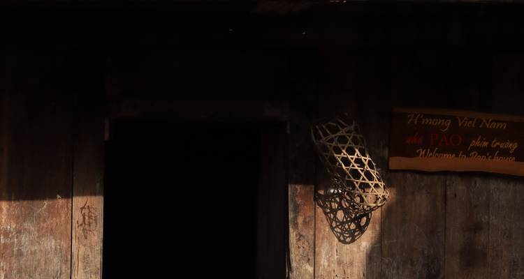 Una entrada de madera poco iluminada con una canasta tejida y un pequeño letrero vietnamita en la pared.