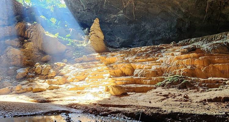 Sonnenstrahlen durchdringen das Dach einer riesigen Kalksteinhöhle und beleuchten terrassenförmig angeordnete Felsformationen.