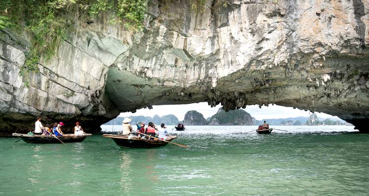 Roeibootjes glijden onder een kalksteen boogpoort door het smaragdgroene water van Ha Long Bay.