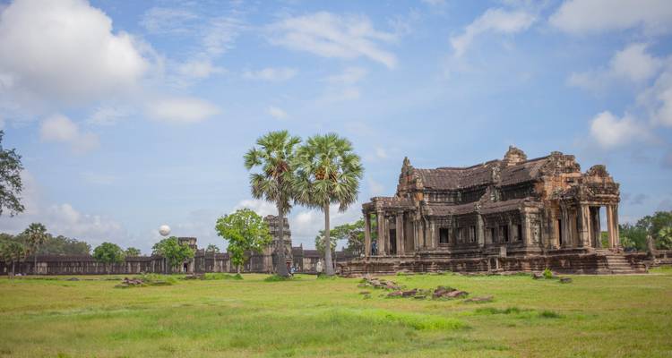 Oude Khmer tempel ruïnes in een grasveld onder een gedeeltelijk bewolkte lucht.