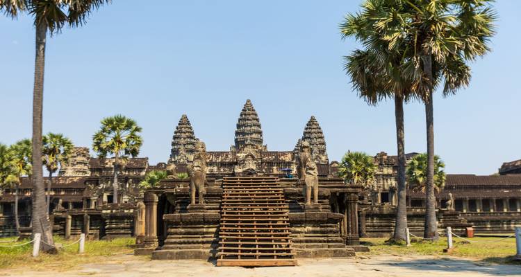 Iconische centrale trap en torens van Angkor Wat omgeven door hoge palmbomen tegen een heldere lucht.