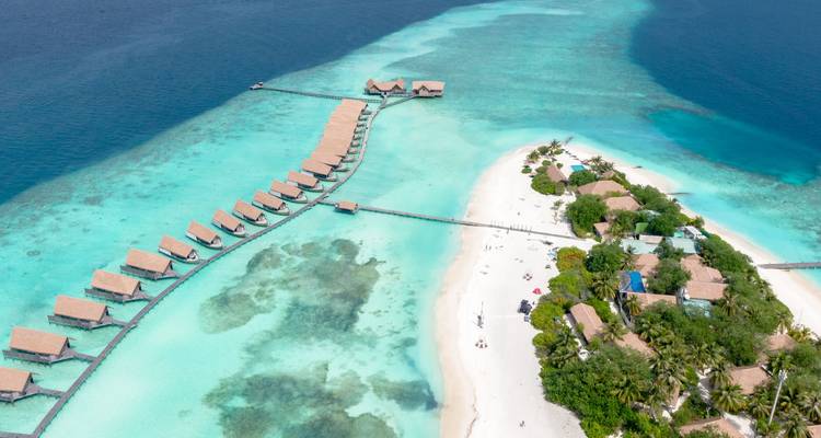 Vue aérienne d'une île tropicale avec une rangée de villas sur pilotis s'étendant dans une mer turquoise éclatante.