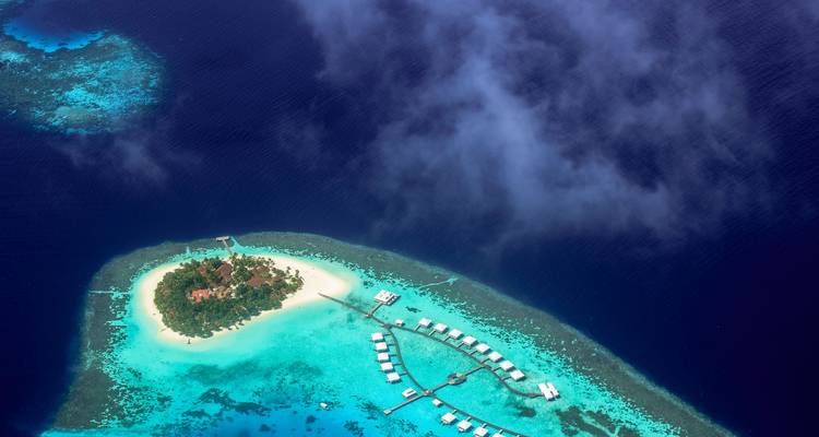 Vue aérienne en haute altitude d'une petite île verdoyante entourée d'un récif bleu turquoise brillant et d'un océan profond et sombre.
