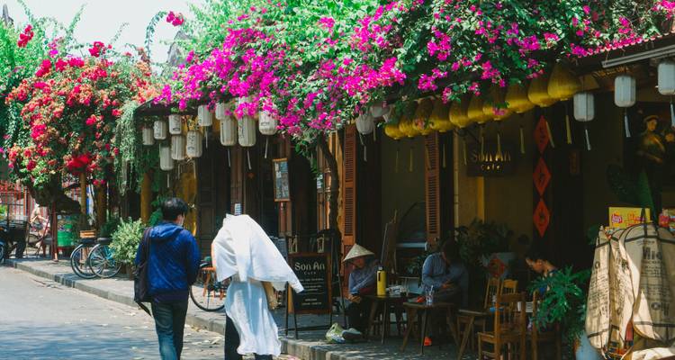 Met bloemen versierde straat in Hoi An met lantaarns en cafébezoekers onder felgekleurde bougainvillea.