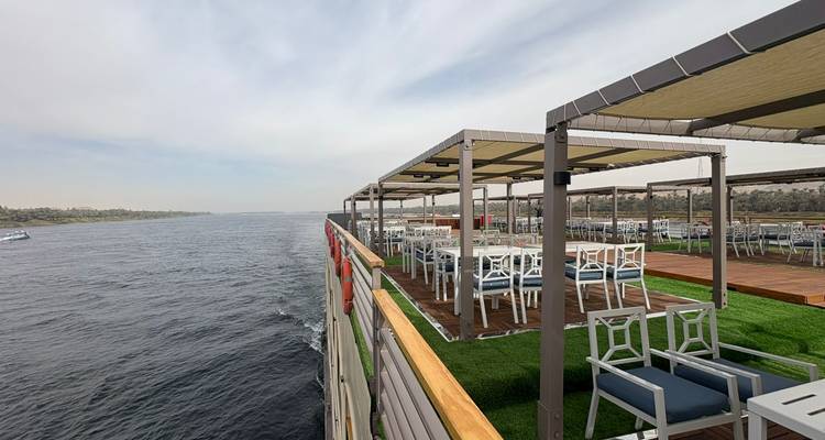 Cubierta abierta en la parte superior de un crucero fluvial con mesas, sillas y césped artificial verde bien organizados que dan a un amplio río tranquilo.