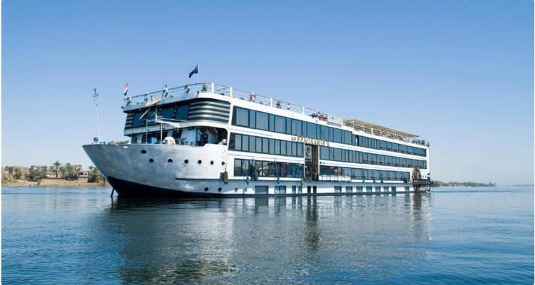 Crucero grande y moderno en el Nilo deslizándose en aguas tranquilas bajo un cielo azul despejado.