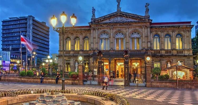 Le théâtre national orné du Costa Rica illuminé au crépuscule avec une fontaine au premier plan.