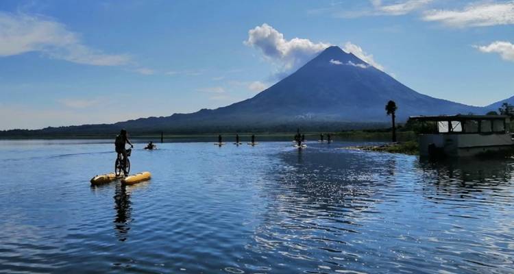 Des aventuriers circulant à vélo nautique sur un lac avec un impressionnant volcan de forme conique en arrière-plan.