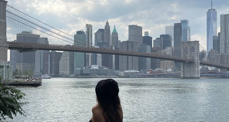 Un visiteur portant un chapeau noir contemple le pont de Brooklyn et la ligne d'horizon de Manhattan de l'autre côté de l'East River.