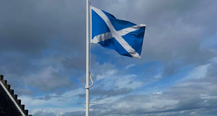 Le drapeau de la Saltire écossaise flottant fièrement devant un ciel dramatique bleu et gris.
