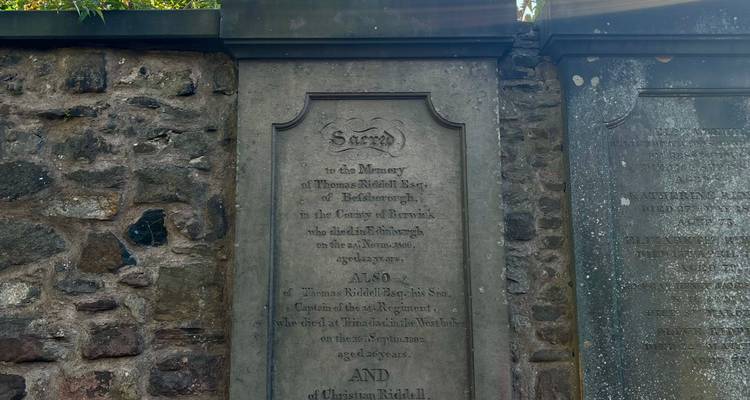 Ancienne pierre tombale aux inscriptions usées, encastrée dans un mur de cimetière en pierre.