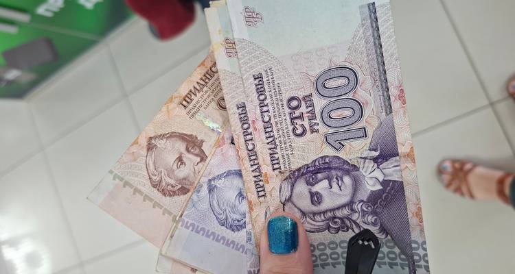 Une main affichant des billets de rouble transnistrien aux couleurs vives dans un cadre intérieur lumineux.