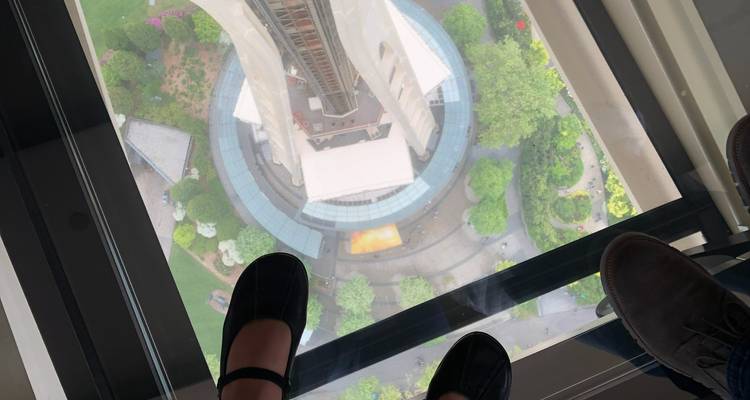 Regardez directement vers le bas à travers le plancher en verre de la Space Needle avec les pieds de deux visiteurs dans le cadre et la base de la tour bien en dessous.