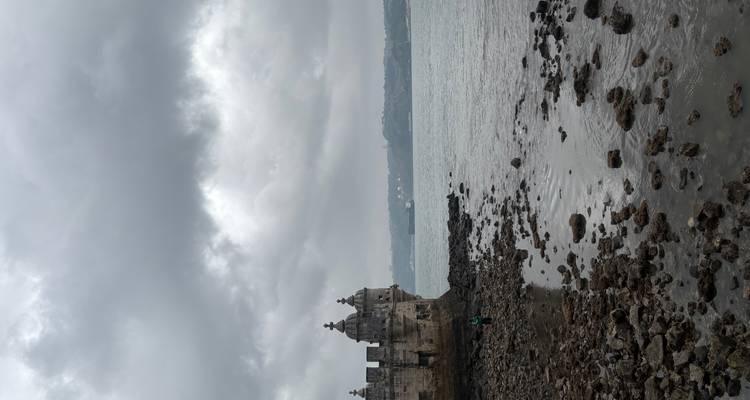 Stone Belém Tower overlooking rocky shoreline and Tagus River under grey clouds