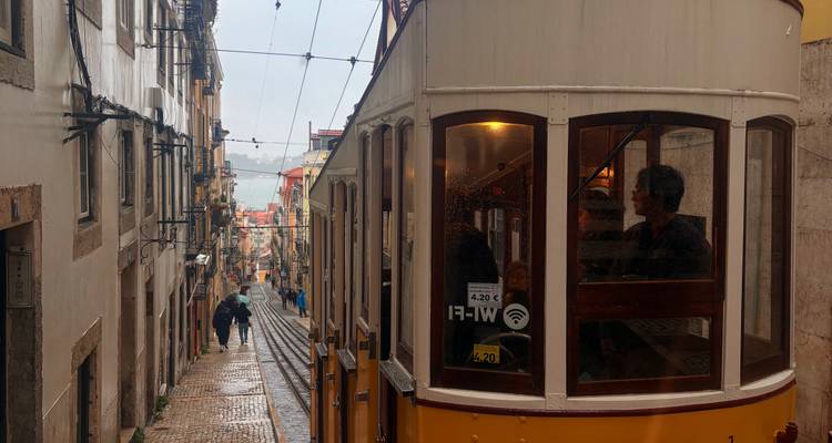 Iconic yellow Bica funicular climbing a steep narrow street in the rain