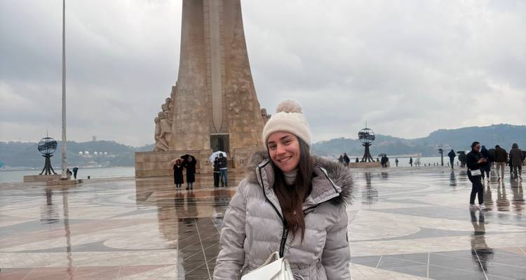 Smiling traveller posing in front of Padrão dos Descobrimentos plaza on a wet day