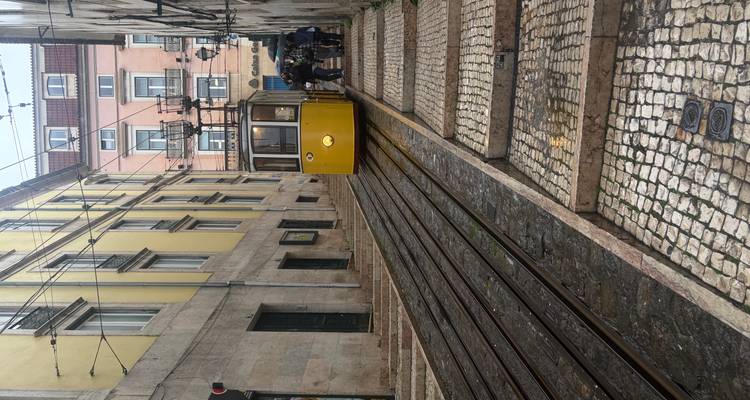 Yellow Lisbon funicular approaching uphill track with passengers waiting in drizzle