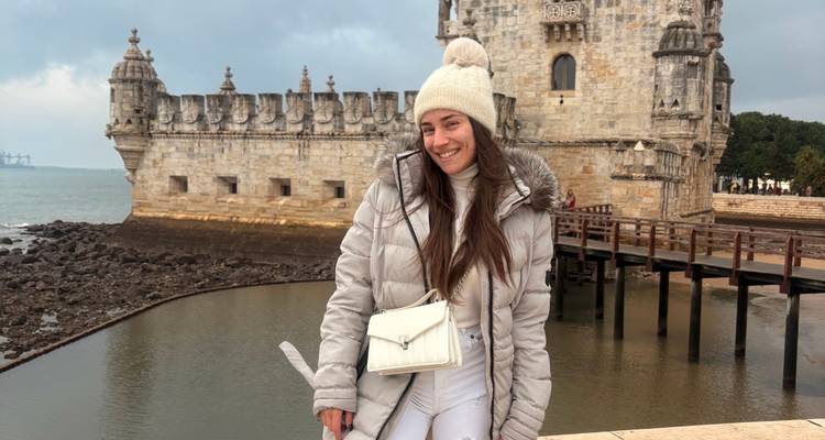 Traveller in white outfit smiling beside Belém Tower and moat