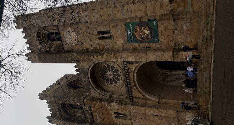 Stone façade of Lisbon Cathedral (Sé) with tour group at the entrance under grey skies