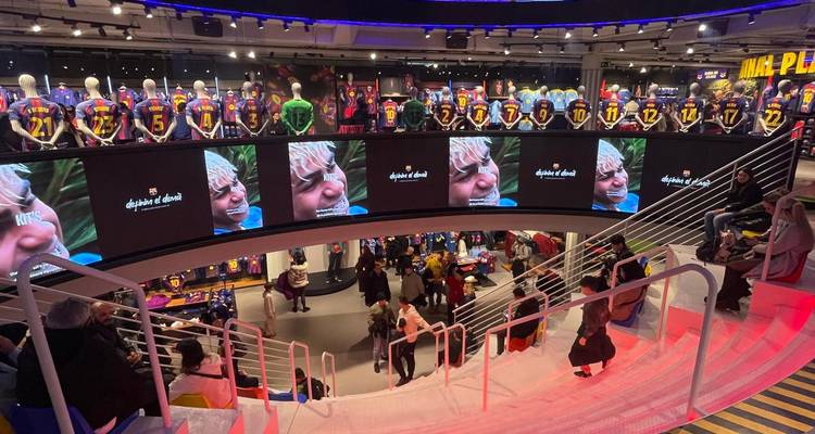 Intérieur de la mégaboutique du FC Barcelona avec des maillots en exposition et des clients sur un escalier courbe