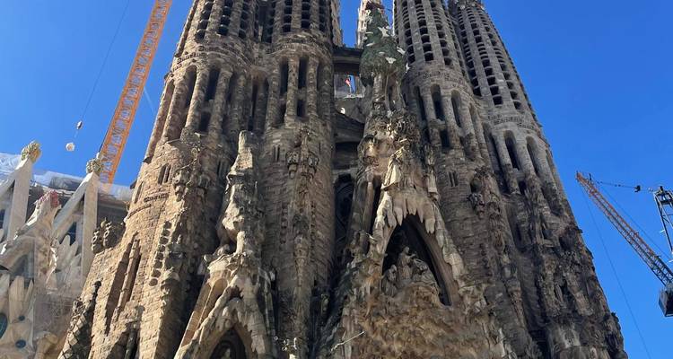 Vue ascendante de la façade de la Nativité de la Sagrada Familia en construction avec des grues sur ciel bleu