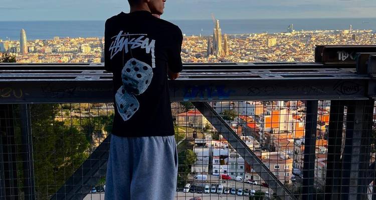 Jeune homme debout à la balustrade d'un point de vue dominant la skyline de Barcelone au coucher du soleil