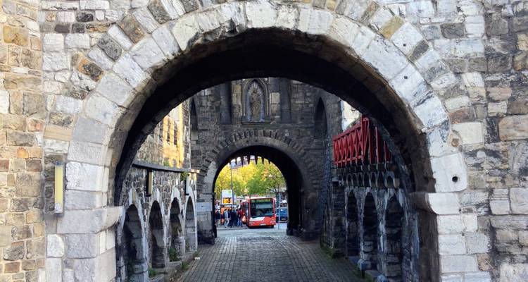 Porte fortifiée médiévale en pierre avec des voûtes en arc encadrant un autobus rouge moderne.