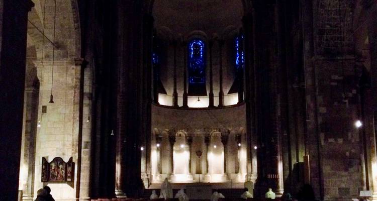 Intérieur de l'abside d'une cathédrale faiblement éclairée avec une petite congrégation en prière.