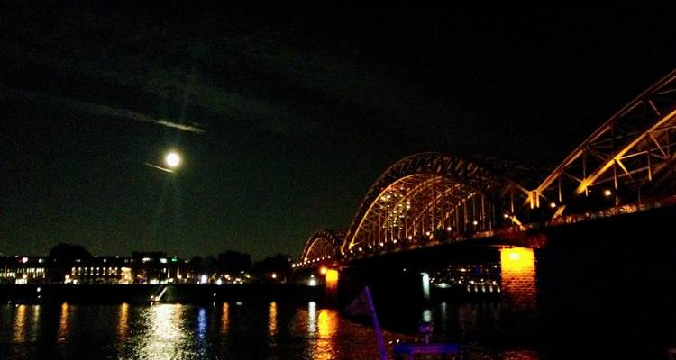 Le pont Hohenzollern illuminé en or la nuit avec la pleine lune se reflétant dans le Rhin.